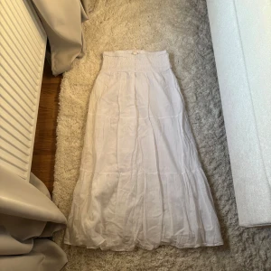 Vit långkjol  - Superfin vit långkjol från Gina Tricot med smock i midjan och lätt volang nertill. Kjolen är luftig och har en flowy känsla, perfekt för varma dagar. Tillverkad i ett tunt och mjukt tyg som känns skönt mot huden. Storlek 170 då den är från gina young❤️