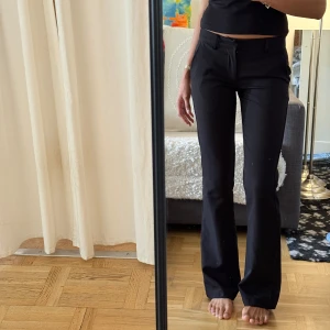Svarta kostymbyxor med bootcut - Snygga svarta kostymbyxor med bootcut-snitt och låg midjade. Byxorna har hällor för bälte, diskreta fickor och stängs med dragkedja och knapp. Perfekta för en clean och stilren look.