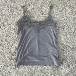 Grå spetslinnetopp från Amisu - Supersnygg grå linnetopp från Amisu med tunna axelband som är justerbara och v-ringning dekorerad med spets. Köpt från newyorker och den är andvänd 1-2 gånger 