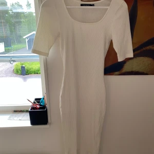 Vit ribbad klänning från Sense Woman - Supersnygg vit ribbad klänning från Sense Woman i figurnära modell. Klänningen har kort ärm, rundad urringning och är tillverkad i ett stretchigt material som sitter perfekt. Enkel och stilren design som är lätt att matcha med accessoarer.