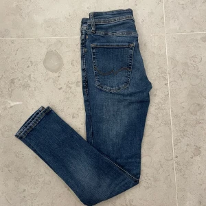 Jack & Jones Skinny jeans blå - Snygga blå skinny jeans från Jack & Jones, modell Liam. Jeansen har klassisk femficksdesign, gul kontrastsöm och en mörk tvätt med lätt slitning. Tillverkade i stretchig bomullsdenim för en tight passform som sitter snyggt hela dagen.