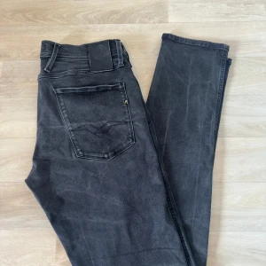 Replay Anbass svarta jeans - Svarta Replay Anbass jeans med snygg tvätt och klassiska fem fickor. Jeansen har raka ben, normal passform och tydliga Replay-detaljer på fickorna. Tillverkade i stretchig denim för extra komfort. Perfekta för en stilren och avslappnad look.