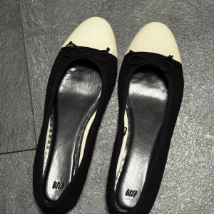 Ballerina skor - Helt nya endast provat dem en gång, dem är för stora för mig och jag kan inte returnera då jag tog bort etiketten. Stilrena ballerinaskor från H&M i svart tyg med vit tå och söt rosettdetalj framtill. Skorna har rund tå och platt sula, perfekta för en chic och enkel look. Passar till både jeans och kjol. Storlek 41. 