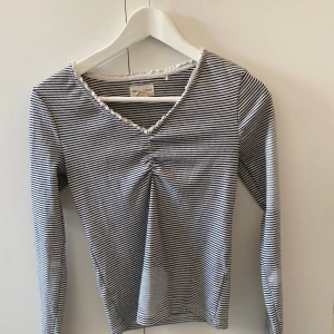Långärmad topp Holly & Whyte - Snygg långärmad topp från Holly & Whyte by Lindex i svartvitt randigt mönster. V-ringad med liten rynkdetalj framtill och diskret volangkant vid halsen.😇