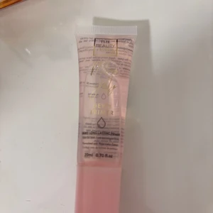 Dewy Primer från The Beauty - Säljer en Dewy Primer från The Beauty i en söt rosa tub på 20 ml. Ger en fräsch, återfuktad finish och funkar perfekt som bas innan smink. Tuben är genomskinlig med guldtext och rosa kork.