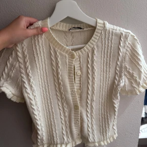 Krämvit stickad blus med knappar - Supersöt krämvit stickad blus med korta ärmar och dekorativa flätmönster från Zara 