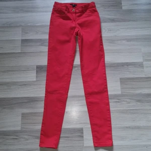 Röda skinny byxor från H&M - Snygga röda byxor från H&M i storlek 34. Modellen är skinny med normal passform och klassisk femficksdesign. Byxorna har gylf med dragkedja och knapp, samt detaljer i guld. Perfekta för dig som vill sticka ut med färg.