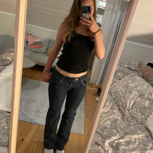 Mörkblå bootcut jeans med låg midja - Säljer ett par mörkblå jeans med bootcut och låg midja. Jeansen har klassiska fem fickor, kontrastsömmar och dragkedja med dubbla knappar. Lite slitna vid skrevet men kommer sy ihop det så bra det går💕Insydda från M till S i benen men passar fortfarande M. Säljer på grund av att de ej kommer till användning längre💖