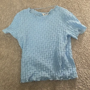 Ljusblå spetsblus från Aware - Supersöt ljusblå blus från Aware i genombruten spets med korta ärmar och vågig kant vid hals, ärmslut och nederkant. Den är köpt från vero Moda. Är tyvärr liten för mig nu.