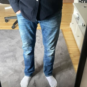  Dundup med slitningar - Säljer ett par blå jeans från dundup med snygga slitningar och dundup-logga baktti lJeansen har normal passform och raka ben, perfekta för en avslappnad stil.