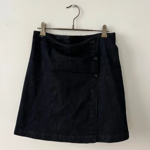 Mörkblå jeanskjol från Boomerang (reversibel) - Supersnygg mörkblå jeanskjol från Boomerang med knappar framtill och plisserad baksida. Kan användas framåt eller bakåt. Kjolen är kort och har en klassisk A-linjeform som ger en stilren vibe. Perfekt att matcha med sneakers eller boots för en cool look.