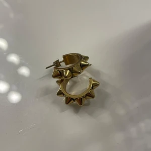 Guldiga örhängen med nitar från Edblad  - Coola guldiga hoops med markerade nitar runt hela örhänget. De har en chunky känsla och ger en edgy vibe till din stil. Perfekta för dig som vill sticka ut och addera lite attityd till din look.