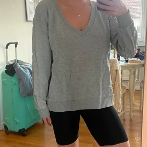 Grå v-ringad tröja från NA-KD - Säljer en enkel och stilren grå tröja från NA-KD i storlek XS. Tröjan har v-ringning, långa ärmar och är gjord i mjuk bomull. Perfekt för en chill och avslappnad look. Passar dig som gillar basic och comfy vibes.