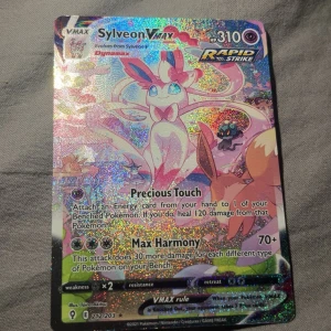 Sylveon VMAX - Glittrande och färgstark Pokémonkort med Sylveon VMAX! Perfekt för samlare och fans av Pokémon TCG. Kortet har coola attacker som Precious Touch och Max Harmony. Ett måste för dig som vill sticka ut i din samling eller i spelet!