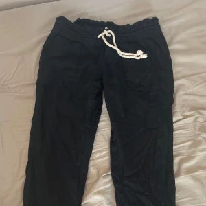 Svarta linnebyxor från Roxy med snörning - Svarta linnebyxor från Roxy med avslappnad passform och bred resår i midjan. Byxorna har begie/vit snörning framtill, fickor både fram och bak samt raka ben. Perfekta för somriga dagar! I storlek M men passar S, Innerbenslängd 83cm.