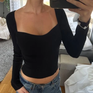 Svart croppad långärmad topp - Säljer en svart, croppad topp med lång ärm och fyrkantig urringning. Toppen är ribbad och sitter tight mot kroppen, perfekt att styla med jeans eller kjol. Enkel men ändå riktigt snygg och trendig.