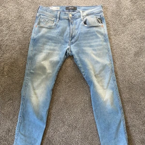 Replay Anbass ljusblå slim jeans - Säljer ett par Replay Anbass Hyperflex jeans i ljusblå tvätt. Slim fit-modell med klassiska fem fickor, snygga slitningar och stretchigt material för extra komfort. Perfekta för dig som gillar en modern och stilren look.