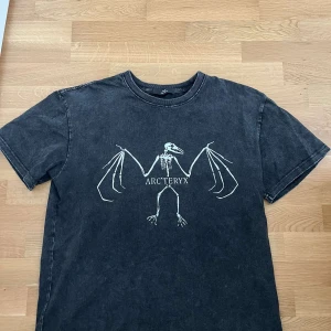 Svart Arc'teryx t-shirt med tryck - Cool svart t-shirt från Arc'teryx med stort vitt skelett-tryck på bröstet. T-shirten har en avslappnad passform, rund hals och korta ärmar. Materialet känns mjukt och vintageinspirerat, perfekt för en streetwear-look.