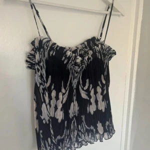 Plisserad svartvit linnetopp H&M M - Säljer en plisserad linnetopp från H&M i svart och vitt med abstrakt mönster. Toppen har smala axelband och volangdetaljer upptill. Luftig och lätt.