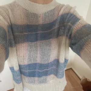 Randig stickad tröja i pastell - Supermysig stickad tröja med breda ränder i ljusblått, beige och ljusrosa. Tröjan har en loose passform, rund halsringning och långa ärmar. Perfekt för dig som gillar en chill och avslappnad stil med pastellvibbar.