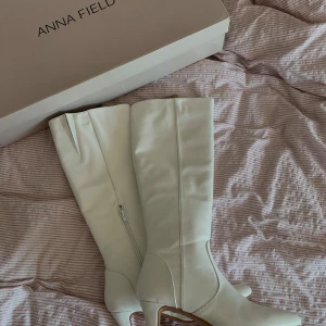 Vita stövlar med klack från Anna Field - Snygga vita stövlar från Anna Field med spetsig tå och smal klack. Stövlarna är knähöga och har dragkedja på insidan. Tillverkade i syntetmaterial med en stilren look som passar perfekt till trendiga outfits.