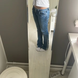 Blå bootcut jeans låg midja - Säljer ett par snygga blå jeans med låg midja och bootcut-modell. Jeansen har klassiska fickor fram och bak, samt snygga slitningar för en cool look. Perfekta till sneakers eller boots och passar dig som gillar en tidlös stil.