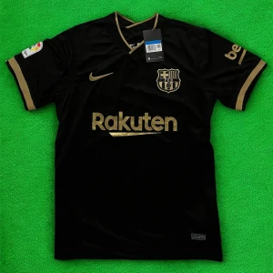 Svart FC Barcelona Nike fotbollströja - Snygg svart FC Barcelona matchtröja från Nike med guldiga detaljer och klubbmärke på bröstet. Rakuten och UNICEF-loggor i guld, samt La Liga-märke på ärmen. Tröjan har V-ringning och är tillverkad i lätt, ventilerande material.