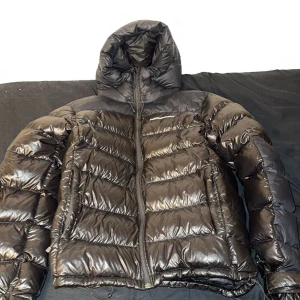 Svart dunjacka Peak Performance M - Säljer en svart, glansig dunjacka från Peak Performance, svårt att hitta denna model idag || Storlek: M|| Skick: 8,5/10|| Mitt pris: 1200kr|| kontakt gärna ifall du har någon fundering🙂