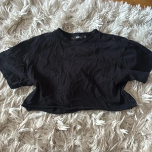 Svart croppad t-shirt från Bik Bok - Enkel svart croppad t-shirt från Bik Bok i mjuk bomull. T-shirten har rund halsringning och korta ärmar.