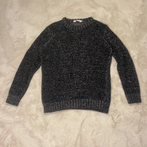 Svartvit stickad tröja  - Mysig svartvit stickad tröja från H&M med grovstickat mönster och ribbade muddar. Tröjan har en klassisk rund halsringning och en svart patch nertill med text. Perfekt för dig som gillar en chill och stilren look.