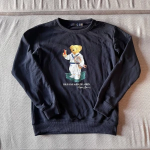 Mörkblå Polo Bear tröja - Säljer en helt oanvänd Polo Bear by Ralph Lauren tröja färgad mörkblå. Tröjan är i storlek M och är i extremt bra skick eftersom den är helt oanvänd. Originalpriset på denna ligger på 3000kr