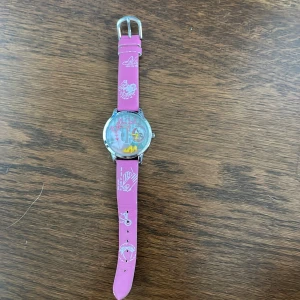 Rosa Elle Girl klocka med motiv - Superfin klocka från Elle Girl med rosa armband och coola vita tryck. Urtavlan har 3D-detaljer som gula klackar, klänning och katt, samt texten 'elleGirl'. Snygg och lekfull accessoar som sticker ut och passar dig som gillar färg och roliga detaljer.