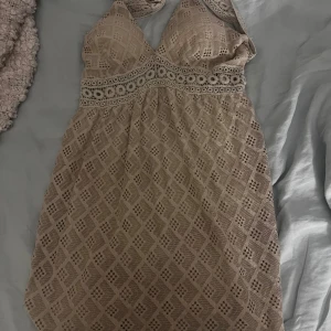 Beige sommarklänning med spetsdetaljer - Supersöt beige sommarklänning med virkade spetsdetaljer och geometriskt mönster köpt i kroatien. Klänningen har halterneck och markerad midja med genombruten spets. Perfekt för sommarens alla tillfällen och ger en bohemisk vibe.