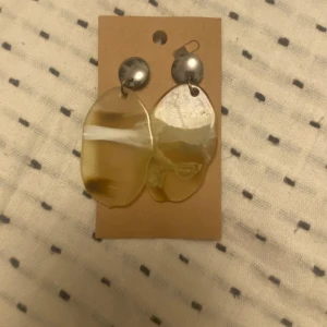 Chunky beige statementörhängen - Stora statementörhängen med rund, silvrig knopp och hängande oregelbunden beige plastdel med vita och bruna inslag. Unik, organisk form som verkligen sticker ut. Ca 7 cm långa och perfekta för att ge din look en cool twist.