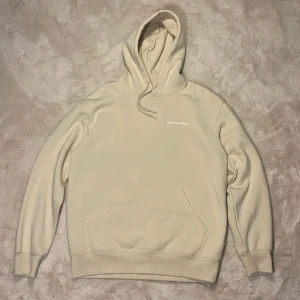 Beige hoodie från H&M - Beige hoodie från H&M med trycket 'IntoTheField' på bröstet och en stor färgglad grafisk print på ryggen. Hoodien har känguruficka, snörning i huvan och relaxed fit. Perfekt för dig som gillar streetwear och snygga detaljer.