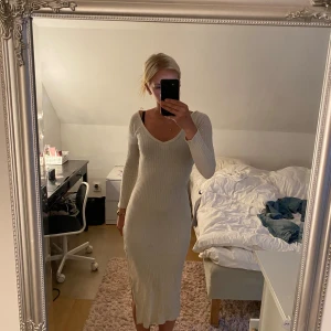 Lång ribbad klänning från Bik Bok - Superfin långklänning från Bik Bok i ljusbeige färg. Klänningen är ribbstickad, har v-ringning både fram och bak samt långa ärmar. Sitter snyggt figurnära och är perfekt för dig som gillar en stilren look. Finns en liten fläck/ prick bak på klänningen men inget man märker av. 