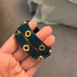 Mörkgrönt läderarmband Tory Burch - Snyggt mörkgrönt armband i läder från Tory Burch. Armbandet är dubbelrads och dekorerat med runda guldfärgade nitar med märkets logga. 