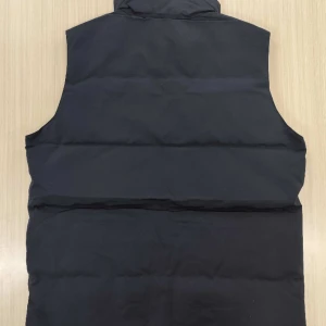 Svart dunväst från Canada Goose - Svart dunväst från Canada Goose, modell Freestyle Crew Vest. Västen har hög krage, två stora framfickor och knäppning med svarta knappar. Klassisk Canada Goose-logga på bröstet och diskret logotyp på ena fickan. 