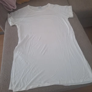 Vit basic t-shirt i bomull - Enkel och stilren vit t-shirt med korta ärmar och rund hals. T-shirten är lång i modellen och tillverkad i mjuk bomull, perfekt för en clean och avslappnad look. Passar dig som gillar minimalistisk stil och vill ha en klassisk bas i garderoben.