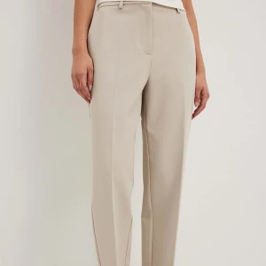 Beigea kostymbyxor från NA-KD - Snygga beige kostymbyxor med raka ben och pressveck från NA-KD. Byxorna har hällor för bälte, diskreta fickor och stängs med dragkedja och knapp. Perfekta för en clean och stilren look. Materialet känns mjukt och har en lätt stretch.