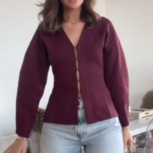 Vinröd kofta - Vinröd kofta med v-ringad hals och smala knappar framtill. Modellen har lång ärm och markerad midja för en snygg siluett. Två av ”spännena” är lite lösa men det medföljer nya om de skulle gå sönder!🥰