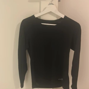 Svart långärmad träningströja Ronhill XS - Svart långärmad träningströja från Ronhill i storlek XS. Tröjan är tillverkad i ett lätt och stretchigt syntetmaterial som andas, perfekt för löpning eller gym. Enkel design med rund hals och diskret logga framtill. Sitter snyggt och är riktigt bekväm.