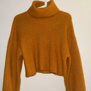 Gul croppad polotröja från Monki - Säljer en croppad, ribbstickad polotröja från Monki i en snygg senapsgul färg. Tröjan har lång ärm, hög polokrage och är gjord i ett mjukt stickat material. Har aldrig använt den. 