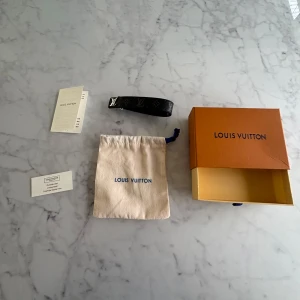 Svart Louis Vuitton armband - Säljer ett svart Louis Vuitton armband med silverfärgat LV-spänne. Armband är gjort i exklusivt skinn med textildetaljer och har en lyxig känsla. Kommer med originalpåse, box och äkthetskort. (Om ni vill ändra priset bara skriv så löser jag något)