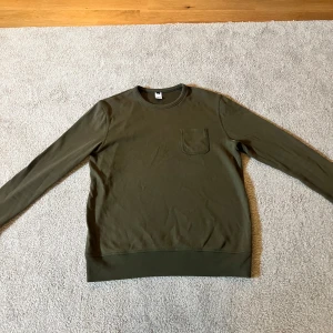 Olivgrön tröja från Visual Clothing Project - Olivgrön långärmad tröja i bomull från Visual Clothing Project. Storlek M.