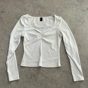 Vit ribbad långärmad topp  - Supersöt vit långärmad topp från Romwe/Shein i ribbat material. Toppen har v-ringning med spetskant och snygg rynkdetalj framtill. Figurnära passform som passar perfekt till jeans eller kjol. Storlek S (EU 36).