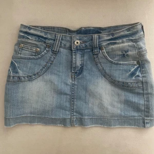 Ljusblå jeanskjol  - Snygg ljusblå jeanskjol från LONNY med klassiska fickor fram och bak, cool broderad detalj på bakfickorna och en liten snörning vid linningen. Perfekt för dig som gillar en avslappnad och trendig stil.