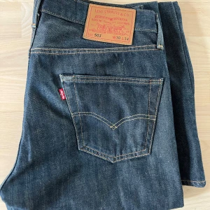 Levi's 501 mörkblå jeans W30 L34 - Klassiska Levi's 501 jeans i mörkblå denim med raka ben och femficksmodell. Snygga kontrastsömmar och ikonisk läderpatch bak i midjan. Perfekta för dig som gillar tidlös stil och vill ha ett par jeans som funkar till allt.