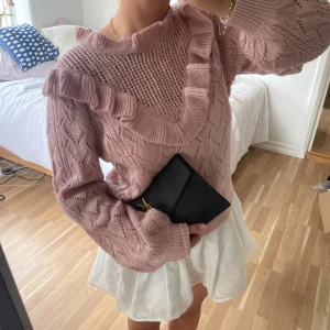 Rosa stickad tröja med volangdetalj💕🥐 - Supersöt stickad tröja i dammigt rosa med volangdetalj längs halsringningen och axlarna. Tröjan har ett snyggt hålmönster och är långärmad med ribbade muddar. Perfekt för dig som gillar romantisk och trendig stil🩷