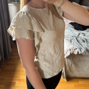 Beige blus med volangärmar från Holly & Whyte - Säljer en beige blus från Holly & Whyte (köpt på Kappahl) med strukturmönster och volangdetaljer på ärmarna. Toppen är i storlek S och köptes förra året. Super söt men aldrig använd och därför säljer jag den nu. Hör av dig vid frågor🫶🏽☺️